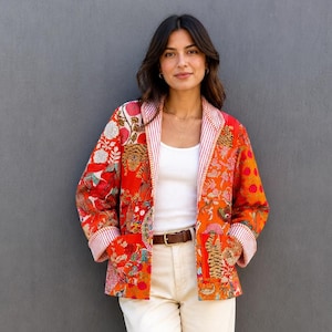 Könnte beinhalten: Eine langärmelige Steppjacke mit einem lebendigen Patchwork-Muster in Rot, Orange und Blumenmotiven. Die Jacke hat ein rot-weiß gestreiftes Innenfutter, umgeschlagene Ärmelbündchen und zwei Vordertaschen, getragen über einem weißen Tanktop und einer cremefarbenen Hose.