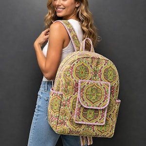 Könnte beinhalten: Ein gesteppter Rucksack mit einem lebendigen, von Paisley inspirierten Muster in Gelb, Grün und Pink. Die Tasche verfügt über eine Vordertasche mit Klappenverschluss, Seitentaschen sowie weiß-pink gestreifte Kanten an Rändern und Trägern.