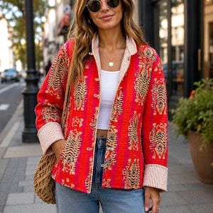 Könnte beinhalten: Eine langärmelige, gesteppte Jacke in leuchtendem Rot und Pink mit einem sich wiederholenden Tigermuster. Die Jacke verfügt über eine Knopfleiste, einen Umlegekragen und breite Ärmelaufschläge, die mit einem weiß-braun gestreiften Stoff gefüttert sind.