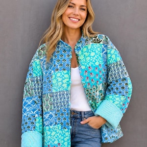May include: A patchwork jacket in shades of blue, teal, and white. The jacket features a variety of floral and geometric patterns, with striped cuffs. The jacket is worn over a white top and blue jeans.