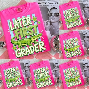 Peut inclure: Plusieurs t-shirts rose vif avec l'inscription "Later First Grader" et un dessin d'alligator vert. D'autres t-shirts affichent "Later Kinder Grader", "Later Pre-K Grader", "Later Second Grader", "Later Third Grader" et "Later Fourth Grader".