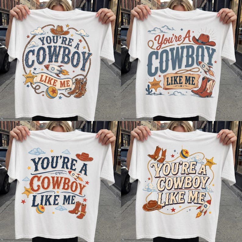 May include: A white t-shirt featuring a graphic print with the text "YOU'RE A COWBOY LIKE ME" in various fonts. The design includes illustrations of a cowboy hat, a rocket ship, a sheriff star, a lasso, a ball, and cowboy boots in colors.