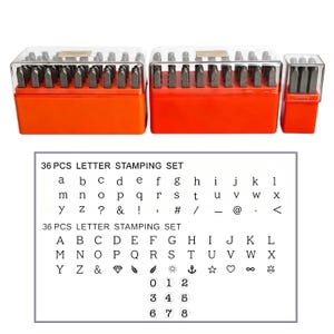 May include: A set of metal stamping tools housed in three orange plastic storage cases with clear lids. The set includes lowercase letters, uppercase letters, numbers, and various symbols such as a diamond, anchor, star, heart, and infinity sign.