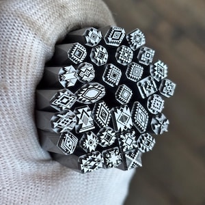 May include: A collection of metal stamping tools bundled together, each featuring a unique geometric pattern on its face. The designs include various combinations of diamonds, triangles, squares, and lines, all rendered in high-contrast black and white.