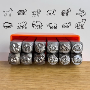 May include: A set of twelve metal stamps arranged in two rows inside an orange plastic holder. Each stamp features a unique animal design on its face, including a dog, tiger, lion, bear, zebra, crocodile, hedgehog, gorilla, elephant, rhino, bull, and wolf.
