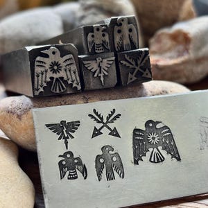 May include: Metal stamps featuring bird designs, including an eagle with outstretched wings and a sunburst. The stamps are shown with impressions on a metal plate, displaying the detailed patterns. These tools are likely used for metalworking or crafting projects.