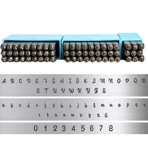 May include: A set of metal stamping tools arranged in three light blue plastic cases, featuring individual steel punches for letters and numbers. Below the punches, three metal strips display the corresponding uppercase letters, lowercase letters, and numbers.