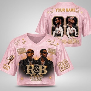 May include: A pink V-neck crop top featuring a graphic print of Chris Brown and Usher, the text "THE R&B TOUR 2026", a microphone, and the number 26. The back displays "YOUR NAME", two images of the artists, the number 88, and "CHRIS & BROWN".