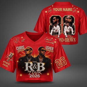 May include: A red V-neck jersey featuring graphic prints of Chris Brown and Usher, the text "THE R&B TOUR 2026," "CHRIS BROWN," "USHER RAYMOND," and "STATE 2026." The back displays "YOUR NAME," the number "26," and two framed photos of a performer.