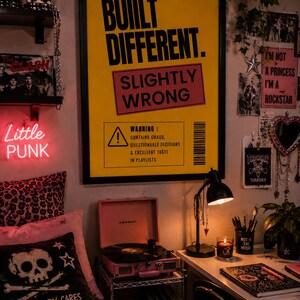 Bold yellow funny typography wall art in a black frame displayed in a punk-inspired teenage bedroom with vinyl records, neon sign, desk, plants, and alternative decor.
