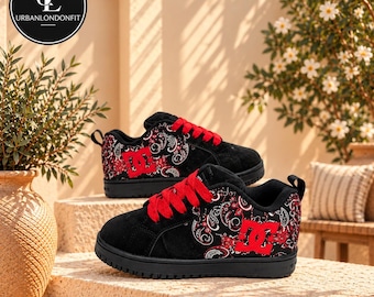 May include: Black DC sneakers featuring a red paisley pattern on the side panels, bright red laces, and a prominent red DC logo. The low-top shoes have a black suede toe cap and a thick black rubber sole, providing a bold contrast.