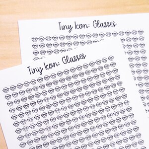 May include: A sheet of paper with the text "Tiny Icon: Glasses" printed at the top. The sheet is filled with small black and white illustrations of glasses.
