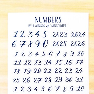 May include: A sheet of white paper with blue numbers printed on it. The numbers are in a handwritten font and range from 1 to 31. The numbers are arranged in rows of seven. The sheet of paper also includes the text "NUMBERS BY J WINSOR @JWINSORART" and "www.judywinsor.com | not for commercial use".