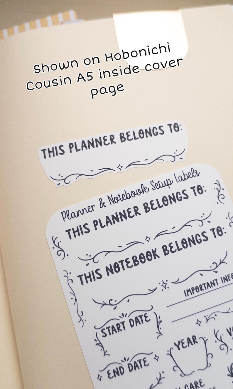 Pode incluir: Etiquetas brancas para configura&ccedil;&atilde;o de planejador e caderno com texto preto e enfeites decorativos. As etiquetas incluem frases como "This Planner Belongs To" e "Start Date". Mostrado em uma p&aacute;gina interna Hobonichi Cousin A5.