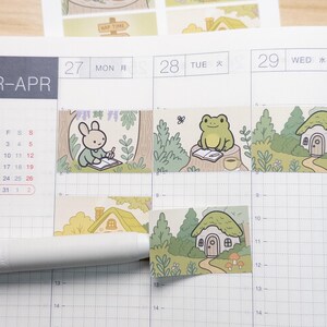 May include: A set of illustrated stickers with a whimsical forest theme. The stickers feature scenes of a bunny writing, a frog reading, and small houses. The color palette includes greens, yellows, and browns, with the text "NAP TIME" visible.
