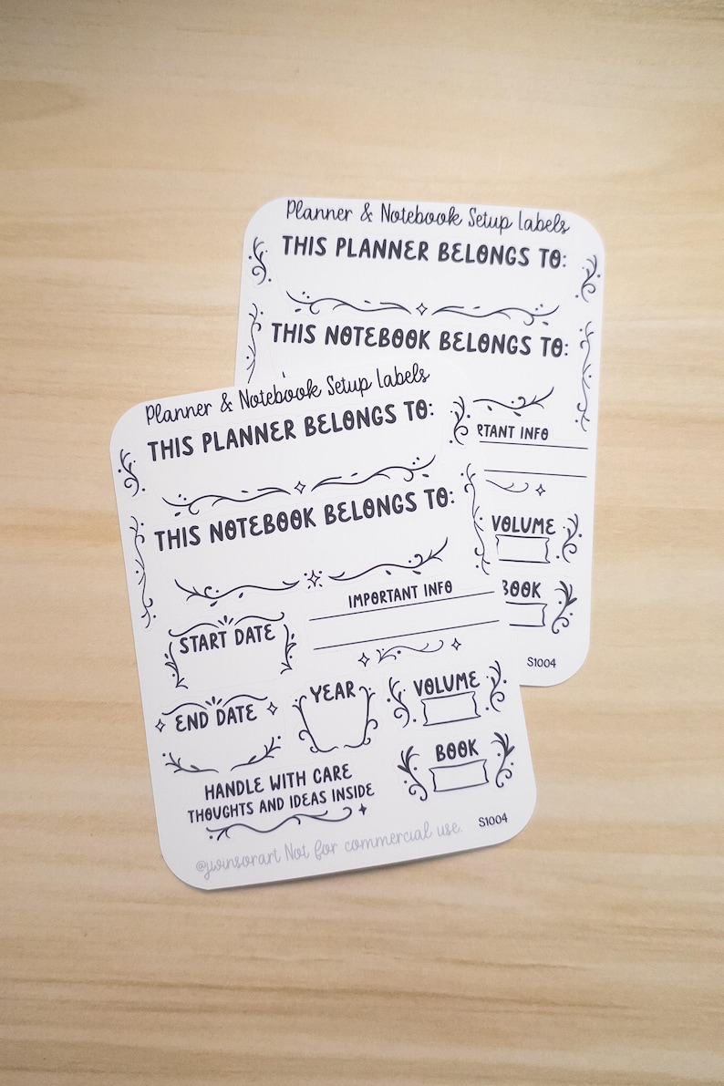 Pode incluir: Duas etiquetas brancas para configura&ccedil;&atilde;o de planejador e caderno com texto preto e enfeites decorativos. As etiquetas incluem solicita&ccedil;&otilde;es para "Este planejador pertence a", "Este caderno pertence a", "Data de in&iacute;cio", "Data de t&eacute;rmino", "Ano", "Volume" e "Livro".