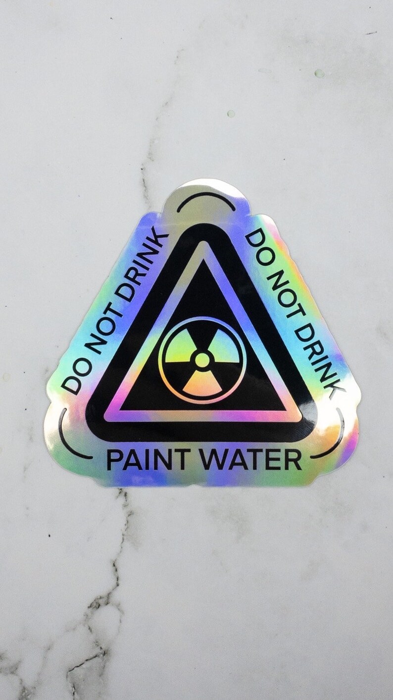 May include: A holographic sticker with a black triangle warning sign. The triangle has a radiation symbol inside and the text "DO NOT DRINK PAINT WATER" around the outside.