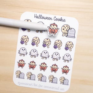May include: A sheet of Halloween-themed stickers featuring cartoon cookies, ghosts, and pumpkin-headed characters. The stickers include the text "Halloween Cookie" and "RIP DIETS". A white pen rests on the sheet.
