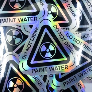 May include: A stack of holographic stickers with a black triangle warning sign. The sign has a radiation symbol and the text "DO NOT DRINK PAINT WATER".