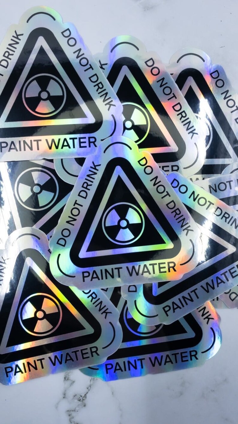 May include: A stack of holographic stickers with a black triangle warning sign. The sign has a radiation symbol and the text "DO NOT DRINK PAINT WATER".