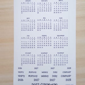 Pu&ograve; includere: Un foglio di adesivi rettangolare bianco con un mini calendario 2027 che inizia di domenica, progettato per il formato Hobo Weeks. Il foglio include dodici griglie mensili da gennaio a dicembre, insieme a etichette di testo per yearly, monthly, weekly, daily.