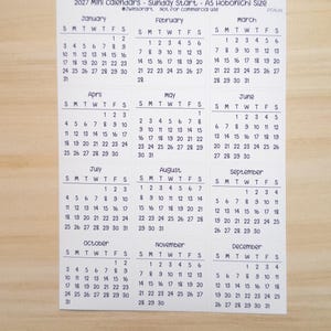 Pu&ograve; includere: Un foglio di carta bianco che presenta un mini calendario 2027 con inizio domenica, etichettato come A5 Hobonichi Size. La griglia mostra tutti i dodici mesi da gennaio a dicembre, ciascuno con le relative date e giorni della settimana in nero.