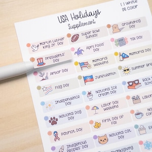 May include: A white USA Holidays Supplement sheet with colorful illustrations and text for various holidays, including Martin Luther King Jr. Day, Presidents' Day, and Independence Day. A pen is partially visible.