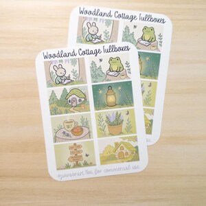 May include: Two sticker sheets with a woodland cottage theme. Each sheet features illustrated panels with a bunny, frog, cottage, lantern, and lavender. Text includes "Woodland Cottage fullboxes", "Nap Time", "Tea Time", and "Mushroom Market".