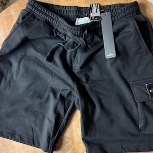 Può includere: Pantaloncini neri con vita con coulisse e una tasca cargo sulla gamba destra. I pantaloncini hanno una piccola toppa con un logo giallo e verde. Un'etichetta è attaccata.