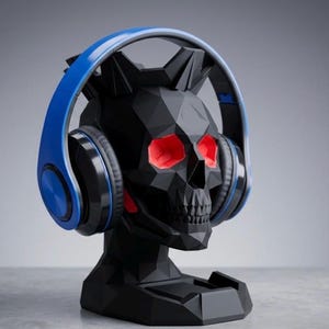 Puede incluir: Soporte para auriculares con forma de calavera negra con cuencas rojas y auriculares azules. El soporte tiene un diseño geométrico y una pequeña base. Un accesorio de escritorio único.