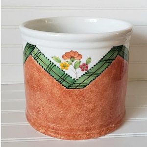 May include: A ceramic planter with a brown and orange glaze. The planter has a green and white plaid design around the top edge with a floral design in the center.