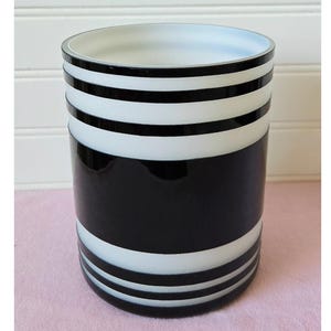 May include: A cylindrical container with a glossy black and white striped design. The container has a wide opening and is suitable for holding various items. The alternating black and white bands create a bold, modern aesthetic.