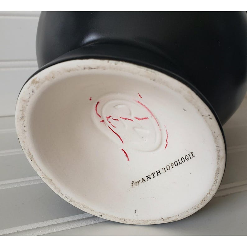 May include: Black ceramic vase with a white base. The base has a red stamp with a logo and the text "for Anthropologie".