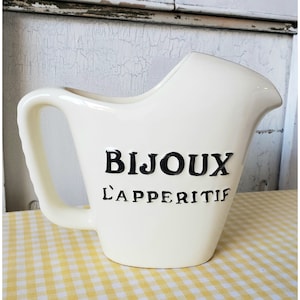 May include: White ceramic pitcher with a black handle and the words "Bijoux L'Apéritif" printed on the front.