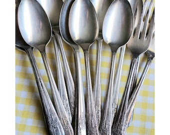 May include: A set of vintage silver spoons with ornate designs. The spoons are arranged in a fan shape, with the handles pointing outwards.