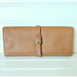 May include: A tan leather wallet with a buckle closure. The wallet is rectangular and has a strap that wraps around it with a silver buckle. The initials "ERM" are embossed on the front.