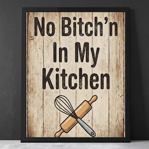 May include: Framed kitchen wall art with the text "No Bitch'n In My Kitchen" in brown letters on a wood-grain background. A whisk and rolling pin are crossed below the text. The frame is black.