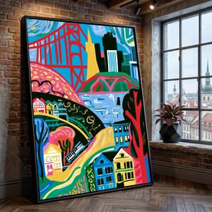 Könnte beinhalten: Ein gerahmter Wandkunstdruck mit einer lebendigen, stilisierten Illustration einer Stadtlandschaft. Das Kunstwerk zeigt eine rote Brücke, einen gelben Wolkenkratzer, bunte Häuser und eine Straßenbahn in einem grafischen Stil mit Blau-, Grün- und Rosatönen.