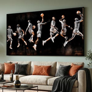 May include: A large framed artwork depicts a sequence of a basketball player in mid-air, executing a jump shot. The player is in a gray and white uniform, set against a dark, textured background. The artwork is displayed above a beige sofa with orange and gray pillows.