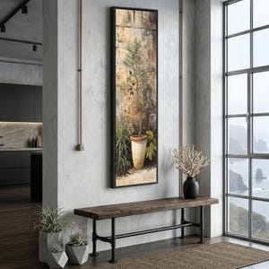 May include: A long, framed print shows an olive tree in a pot against a textured wall. The artwork hangs above a wooden bench with black metal supports. The room has a neutral colour scheme, with a large window offering a coastal view. The bench is approximately 150 cm long.