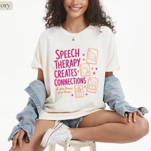 Puede incluir: Una camiseta color marfil con el texto rosa "SPEECH THERAPY CREATES CONNECTIONS" y el texto naranja "if you know, you know". El diseño incluye ilustraciones naranjas de cartas de juego con iconos relacionados con el habla y estrellas.