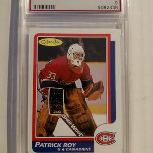 May include: A graded 1986 O-Pee-Chee Patrick Roy hockey card. The card shows a colour image of Roy in his Montreal Canadiens uniform. The card is encased in a protective case, with the grade and serial number visible.