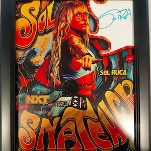 May include: Framed poster featuring Sol Ruca, with vibrant red, orange, and yellow text that reads "Sol Snatch". The image includes a signature and the NXT logo. The poster is framed in a black frame.