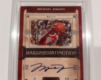 Może przedstawiać: Karta kolekcjonerska Michaela Jordana z serii 2006 SP Signature Marks of Distinction. Karta zawiera wizerunek Jordana w stroju Bulls, jego podpis i tekst "AUTHENTIC AUTO 10". Karta jest umieszczona w ochronnym etui.