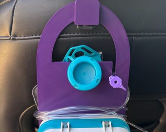 May include: A purple 3D-printed plastic holder hanging from a car headrest, supporting a teal and white Infinity by Moog enteral feeding pump. The device features a digital display, control buttons, and clear tubing connected to a teal cap.