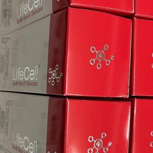 Op de afbeelding: Gestapelde dozen met LifeCell South Beach Skincare producten. De dozen zijn rood en grijs, met de merknaam en het logo. De rode dozen hebben een zilveren design.