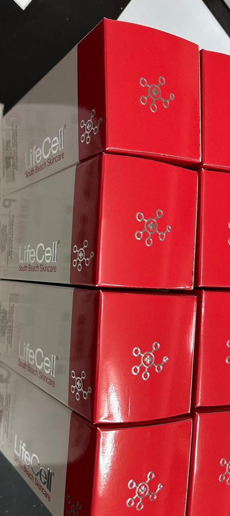 Op de afbeelding: Gestapelde dozen met LifeCell South Beach Skincare producten. De dozen zijn rood en grijs, met de merknaam en het logo. De rode dozen hebben een zilveren design.