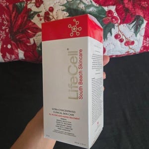 K&ouml;nnte beinhalten: Eine wei&szlig;e und rote Schachtel von LifeCell South Beach Skincare. Die Schachtel tr&auml;gt den Text &bdquo;Ultra-konzentrierte klinische Hautpflege All-in-One Anti-Aging-Behandlung&ldquo;. Die Schachtel wird vor einem festlichen rot-wei&szlig; gemusterten Hintergrund gehalten.