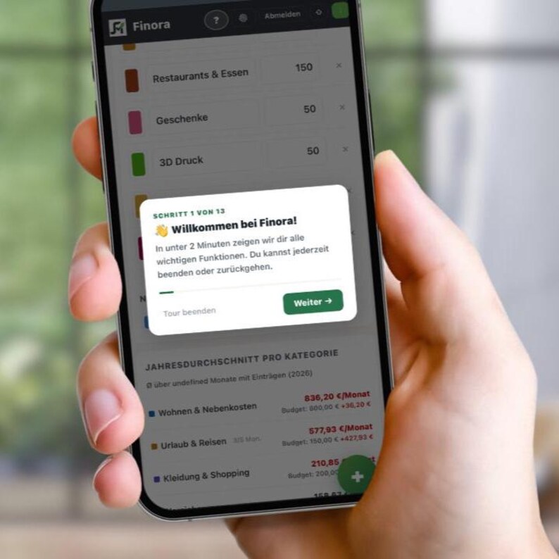 May include: A smartphone screen showing the Finora app interface. The app displays a welcome message in German, and budget categories such as "Restaurants & Essen" and "Kleidung & Shopping." The interface has a modern design with a green and white colour scheme.