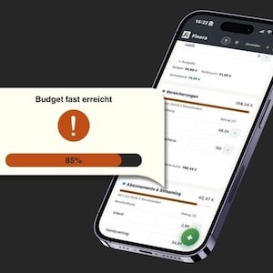 May include: A smartphone screen showing a finance app interface with a warning message: "Budget fast erreicht" (Budget almost reached). The screen displays spending details and a progress bar at 85%.